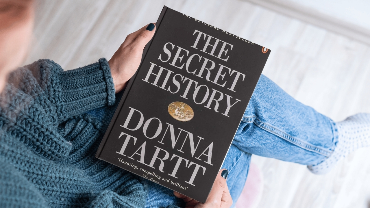 Osoba drži knjigu „The Secret History“ od Donne Tartt dok sedi